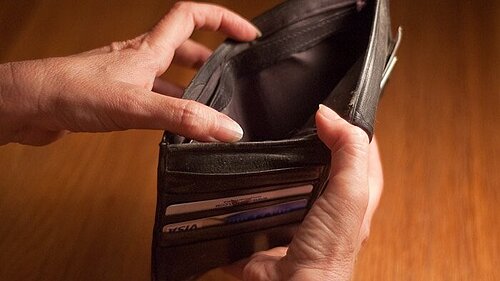 A person opening a wallet to reveal it is empty.